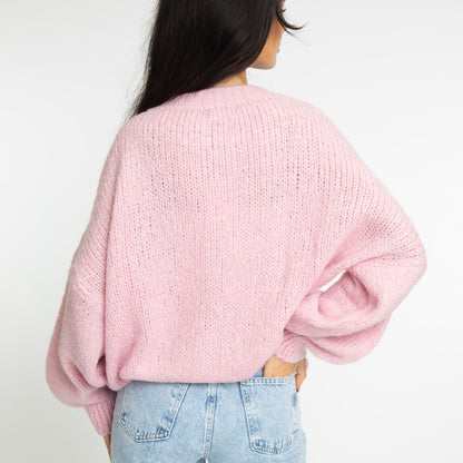 Person wearing a pink sweater and light blue jeans on a white background