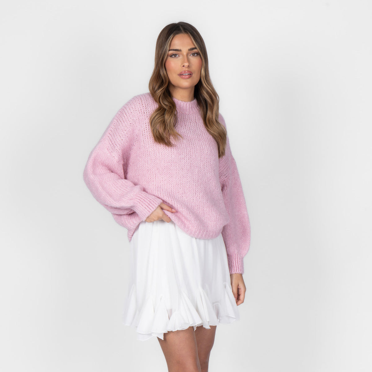 Woman wearing a pink sweater and white skirt on a plain background
