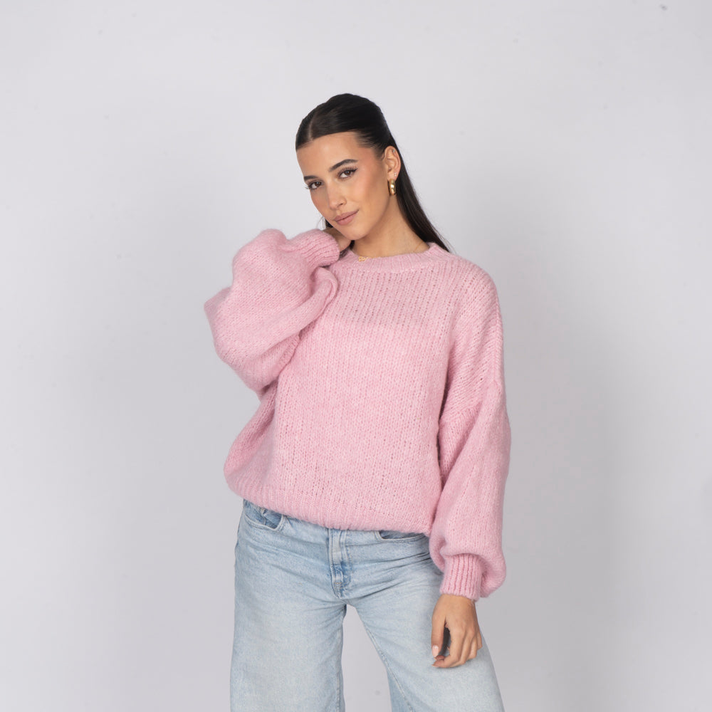 Woman wearing a pink sweater and light blue jeans against a plain background
