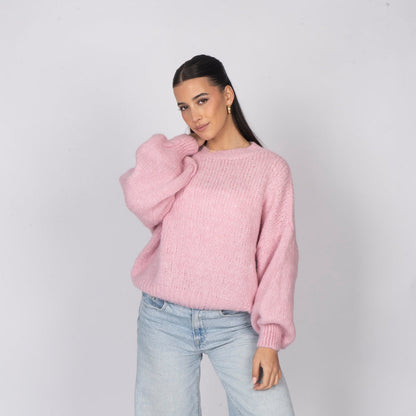 Woman wearing a pink sweater and light blue jeans against a plain background