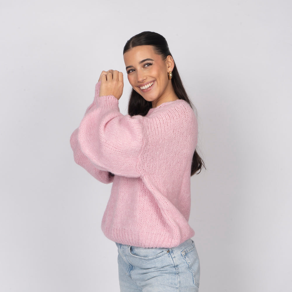 Woman wearing a pink sweater and light blue jeans against a plain background