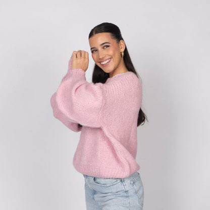 Woman wearing a pink sweater and light blue jeans against a plain background