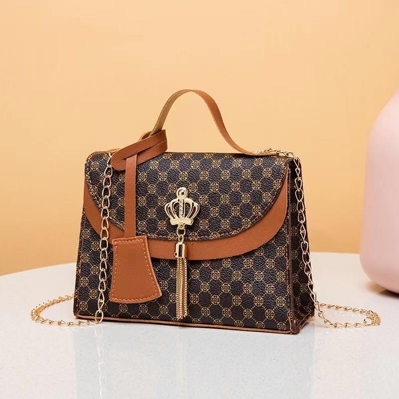 Designer handbag with patterned design and gold chain on a light blue surface.