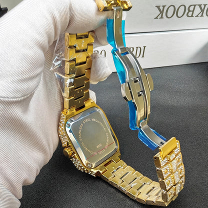 Gold watch with a unique design held by a gloved hand on a dark surface.