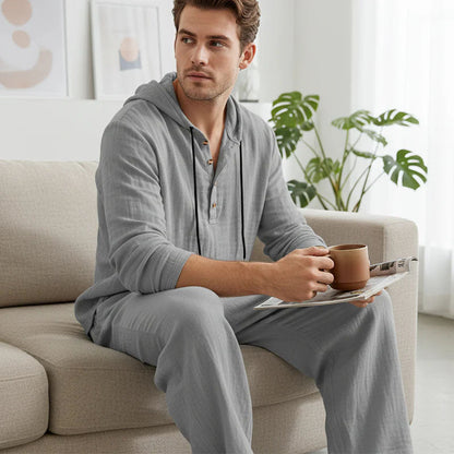 Man in gray pajamas sitting on a couch holding a mug and reading a magazine in a cozy living room.