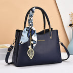 Navy handbag with floral scarf and leaf charm on a beige background