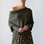 Person wearing an off-shoulder green sweater with a plain background