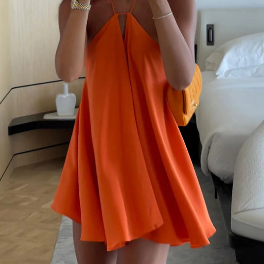 Person wearing an orange dress holding a yellow handbag in a bedroom setting.