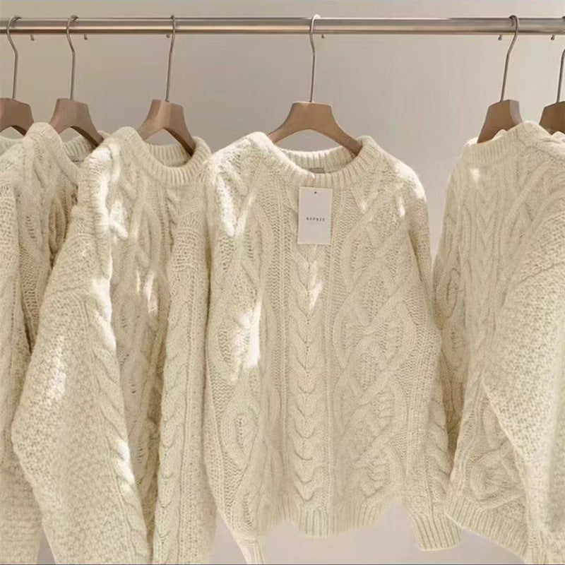 Row of cream-colored cable knit sweaters on hangers with a visible brand tag.