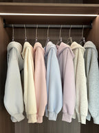 Row of pastel-colored hoodies hanging on a rack in a wardrobe.