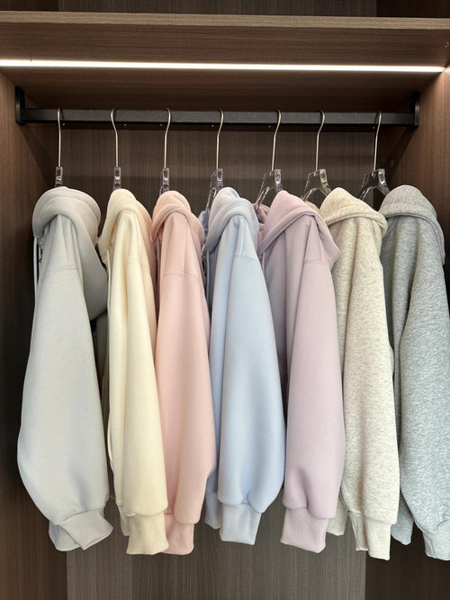 Row of pastel-colored hoodies hanging on a rack in a wardrobe.