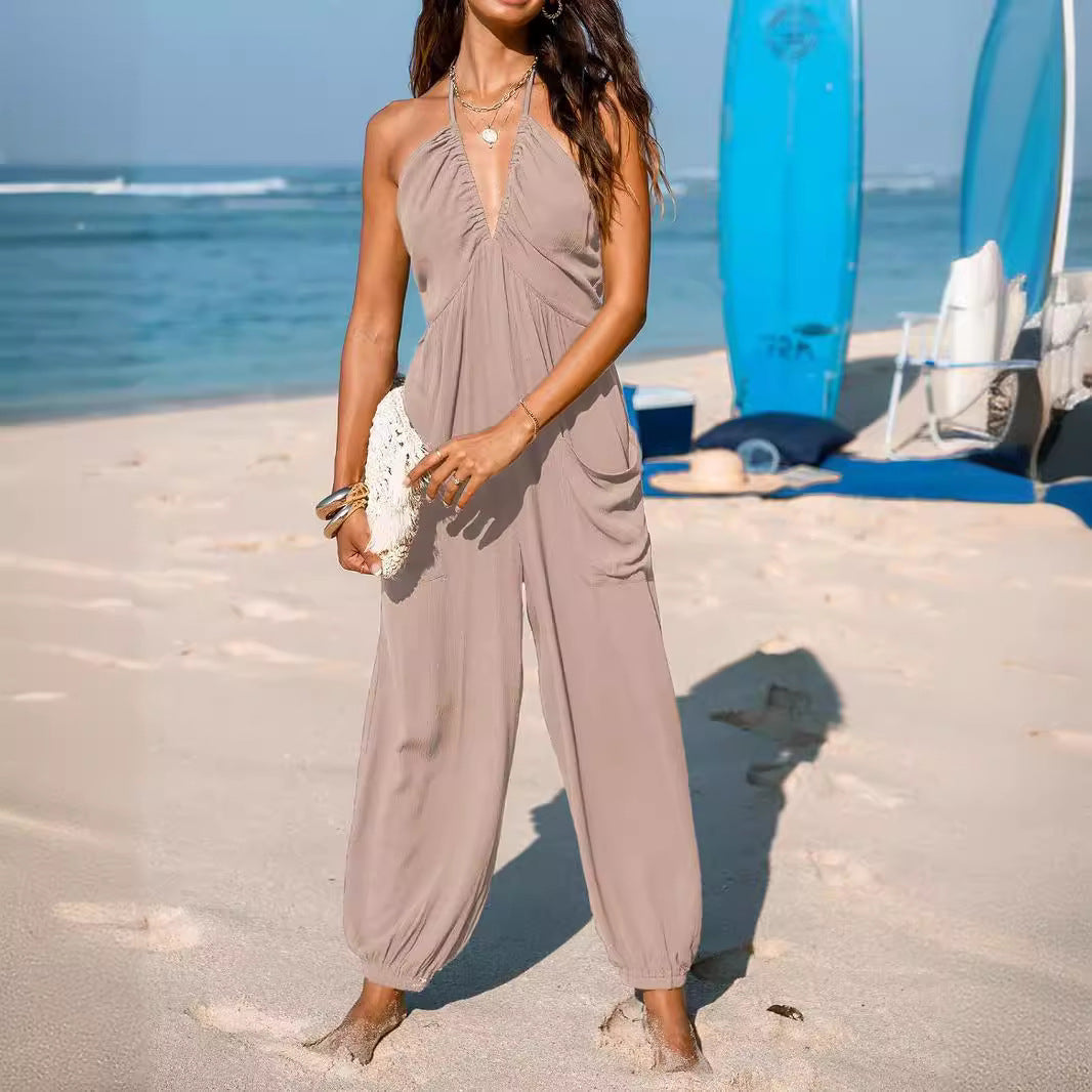 Woman in a beige jumpsuit standing on a beach with boats in the background