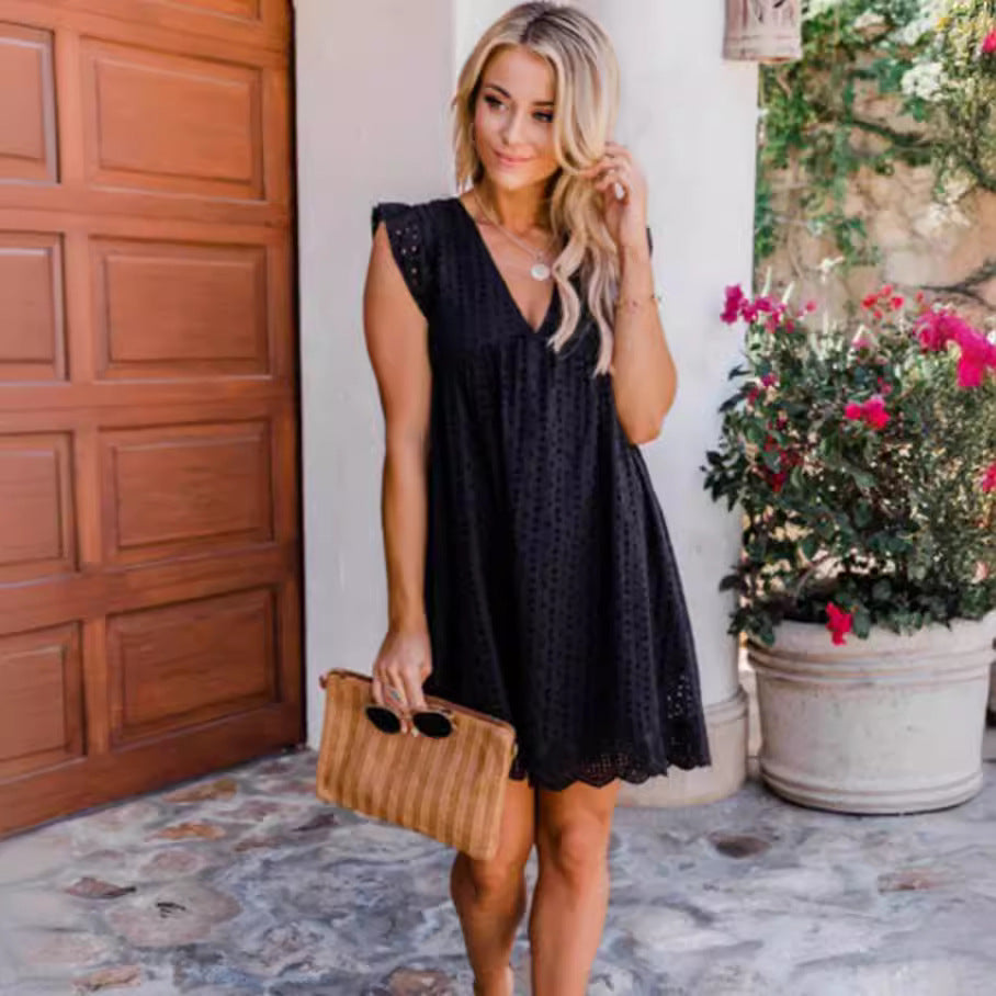 Woman in a black dress holding a brown clutch in front of a wooden door and potted plant.