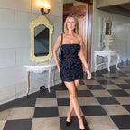 Woman in a black dress standing in a room with checkered floor and decorative mirrors.