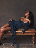 Woman in a blue dress sitting on a wooden bench against a dark background