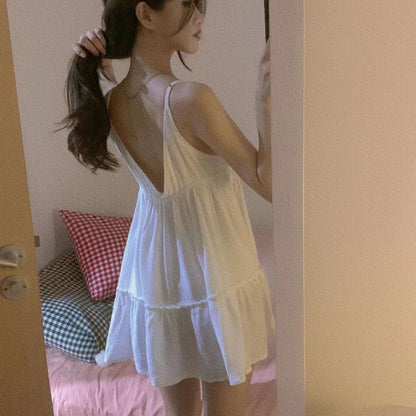 Woman in a white dress standing in a room with a bed and pillows.