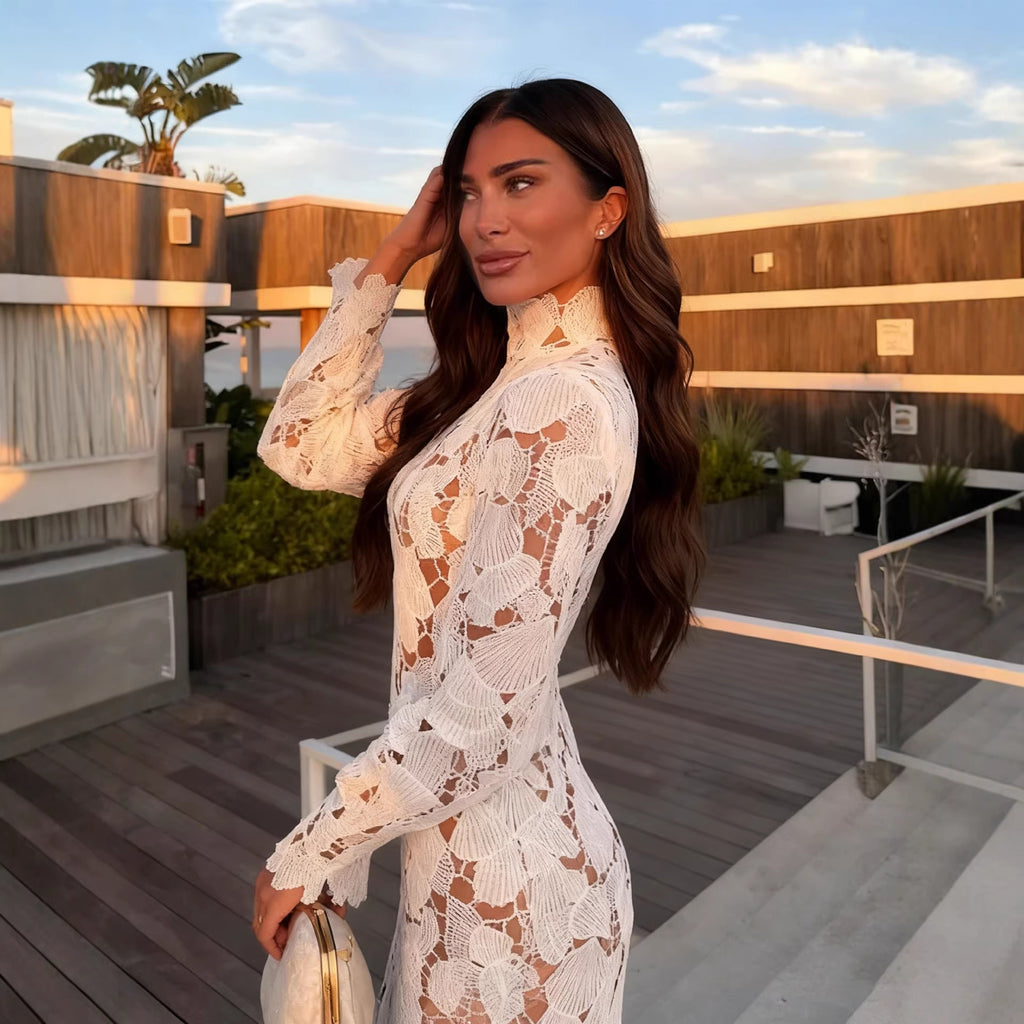 Woman in a white lace dress standing on a rooftop with wooden deck and plants.