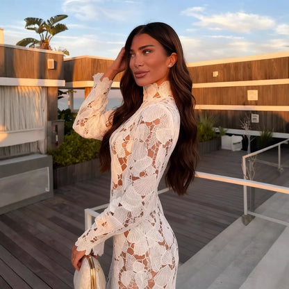 Woman in a white lace dress standing on a rooftop with wooden deck and plants.