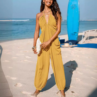 Woman in a yellow jumpsuit standing on a beach with ocean and blue surfboard in the background