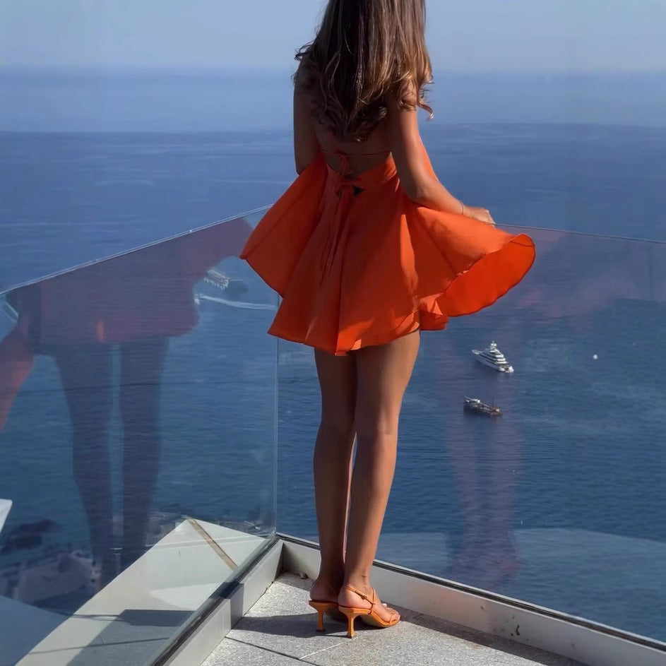 Woman in an orange dress standing on a balcony overlooking the ocean with boats.