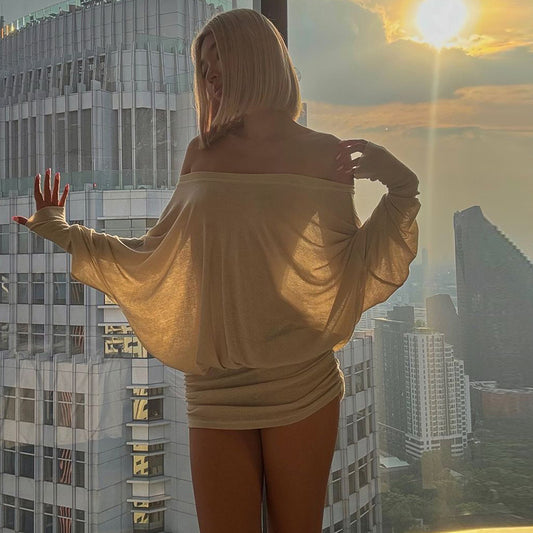 Woman standing on a balcony with a cityscape view during sunset.