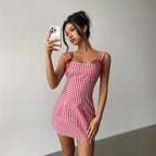 Woman taking a selfie wearing a red and white checkered dress against a plain background