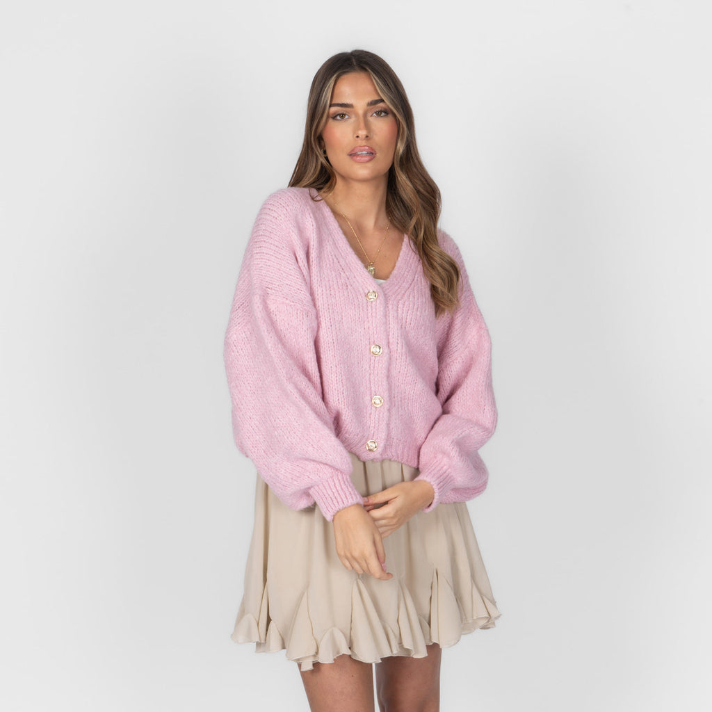 Woman wearing a pink cardigan and beige skirt on a white background