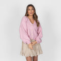 Woman wearing a pink cardigan and beige skirt on a white background