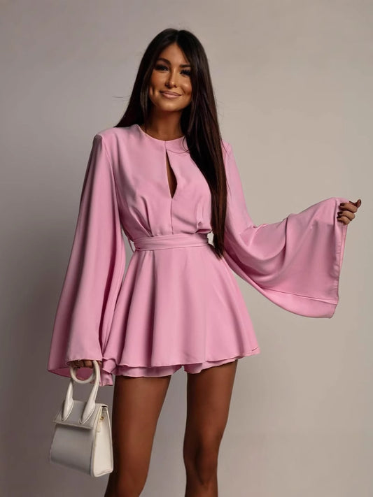 Woman wearing a pink dress with wide sleeves against a plain background