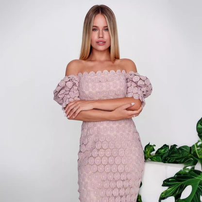 Woman wearing a pink lace dress with a white background and green plant.