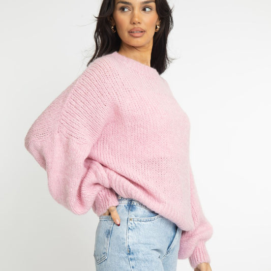 Woman wearing a pink sweater and light blue jeans on a white background