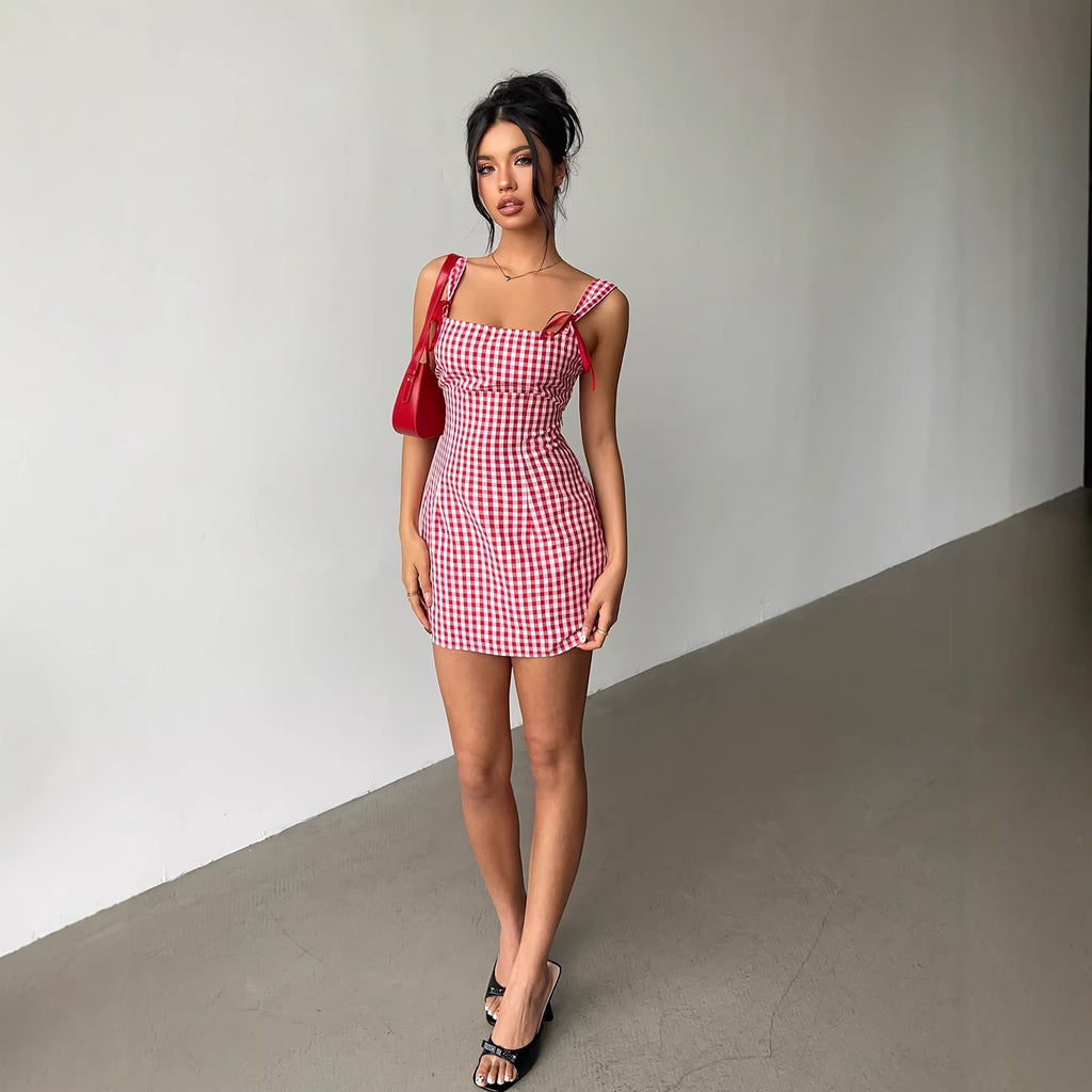 Woman wearing a red and white checkered dress with a red bag against a plain background
