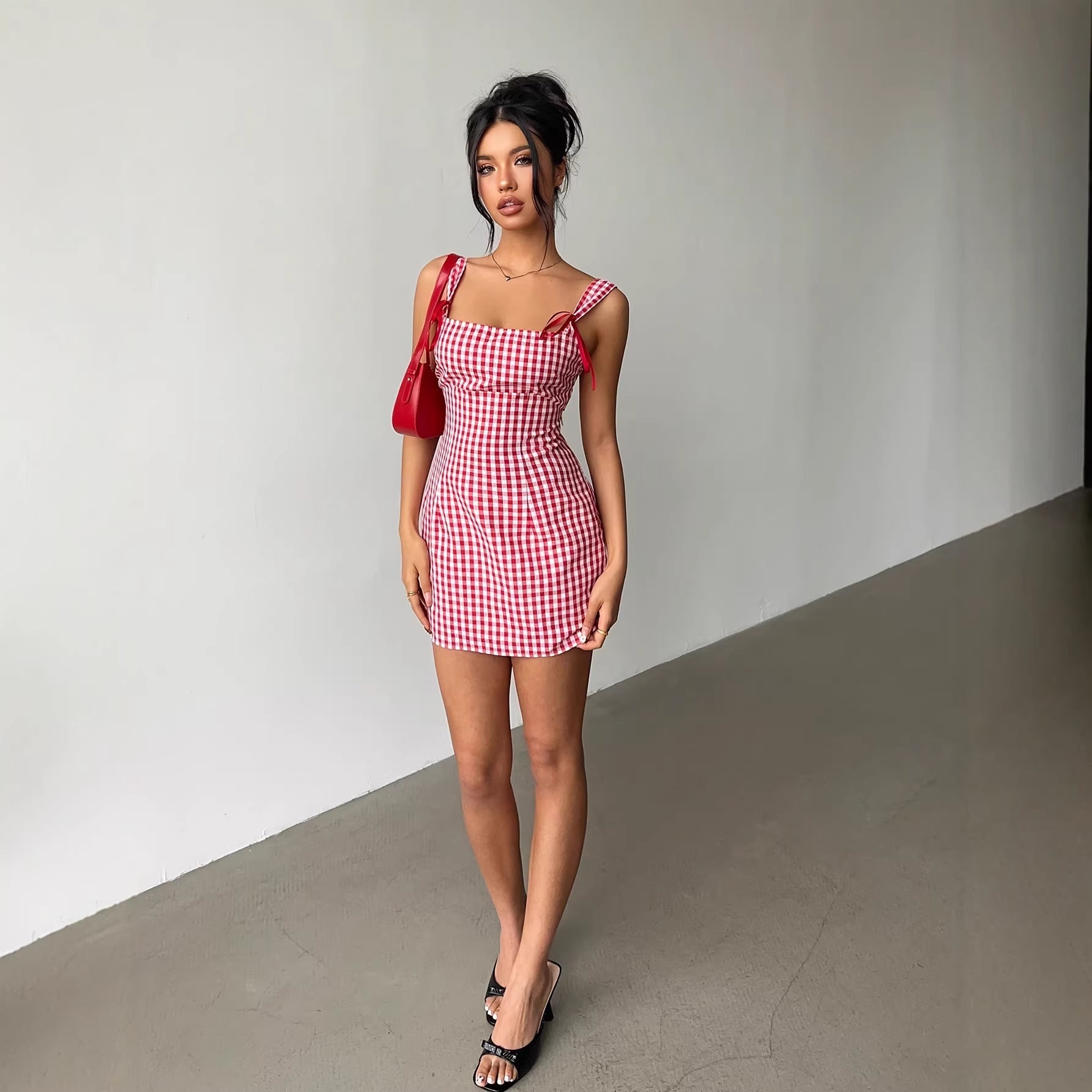 Woman wearing a red and white checkered dress with a red bag against a plain background
