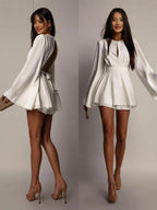 Woman wearing a white dress with long sleeves on a plain background