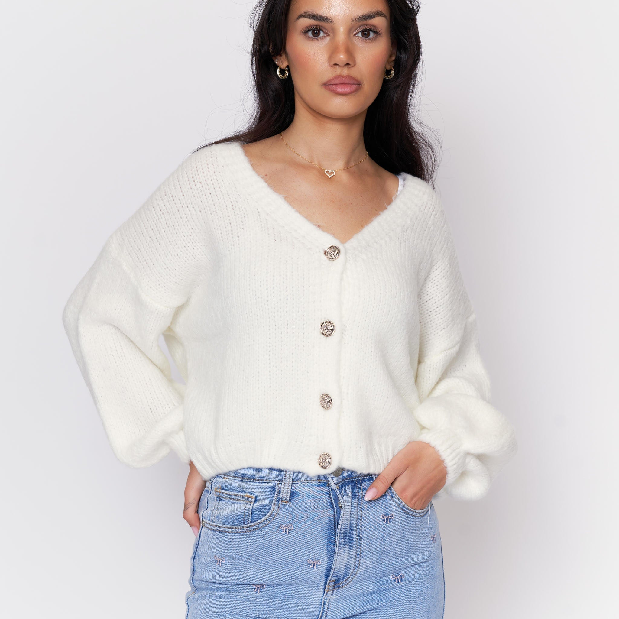 Woman wearing a white cardigan with button details on a plain background