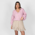 Woman wearing a pink cardigan and beige skirt on a white background
