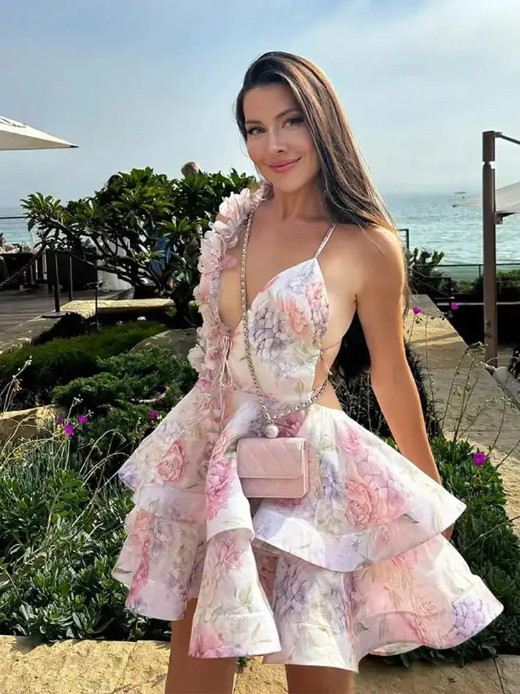 Woman in a floral dress with a matching handbag standing outdoors near the ocean.