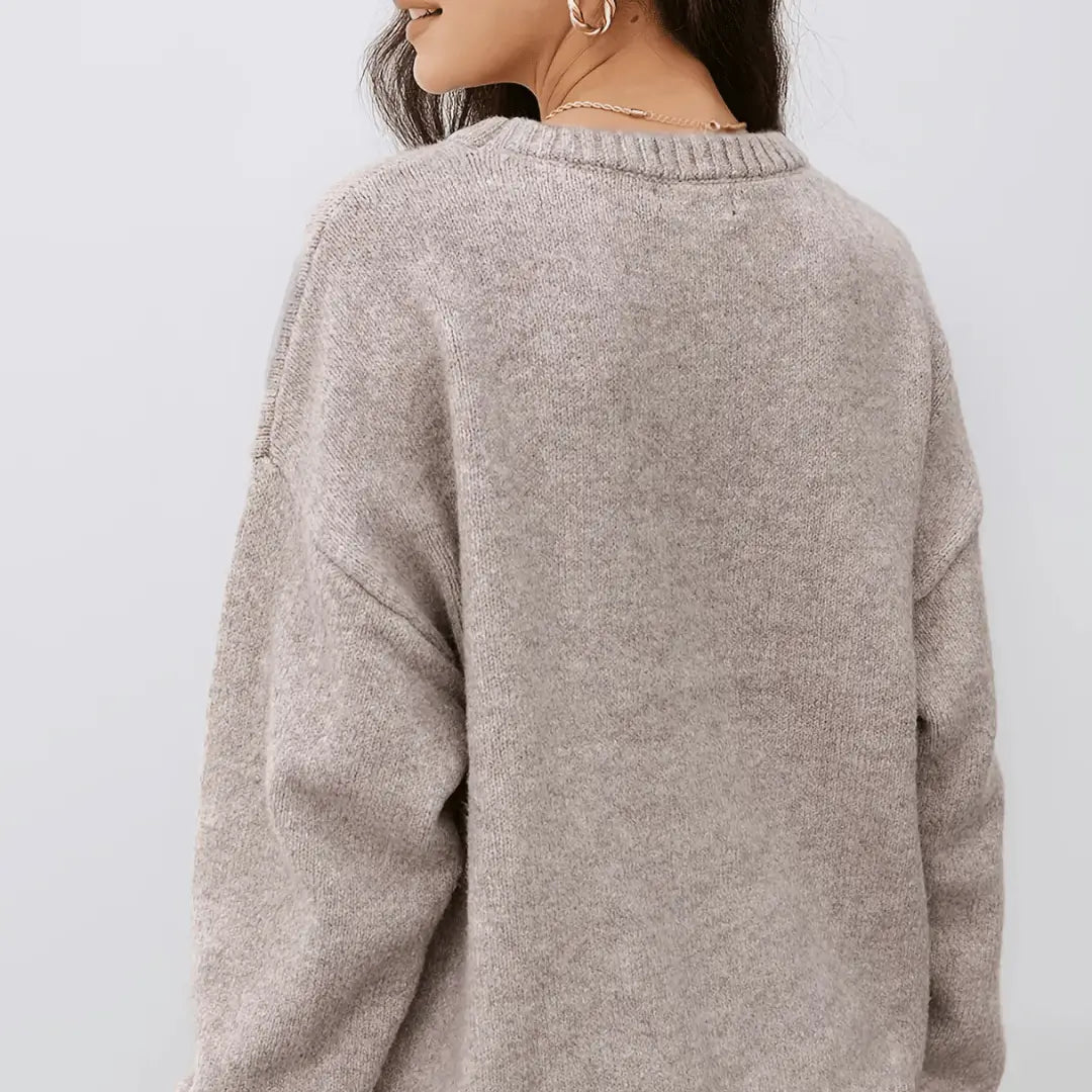A close-up back view of a woman wearing a soft, heathered taupe knit sweater against a light gray background.